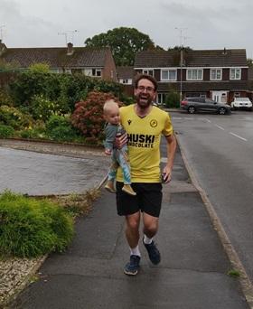 Man in football shirt running down the street carrying his baby