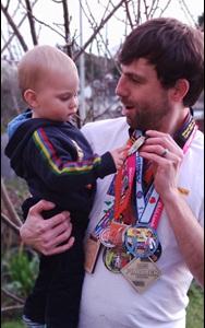 Man holding a baby who is looking at the medals around his neck