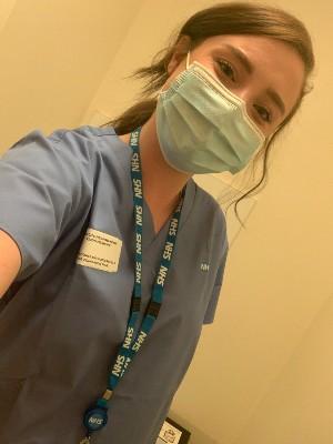 Young white woman wearing a facemask, scrubs and NHS lanyard