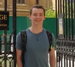 Young man wearing t-shirt and rucksack in front of metal gates