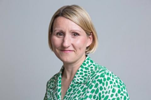 White woman with short blonde hair. She is wearing a green and white patterned shirt.