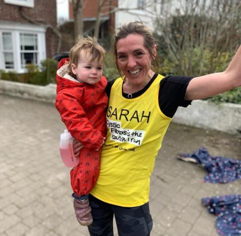 Sarah wearing a CF Trust yellow running vest for Running Festival holding her daughter