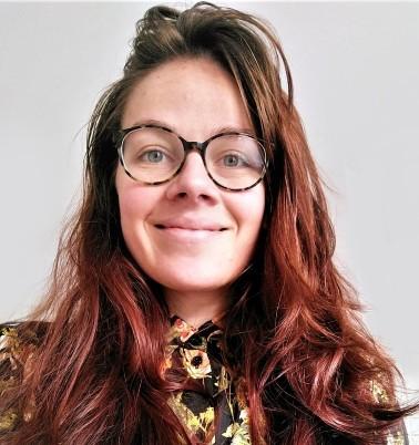 Young white woman wearing glasses and patterned black shirt. She is smiling.