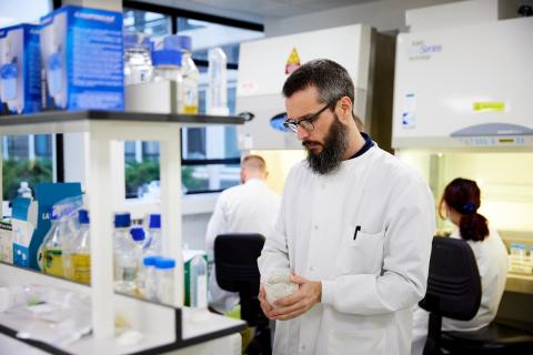 Man in lab coat is inspecting a jar of liquid