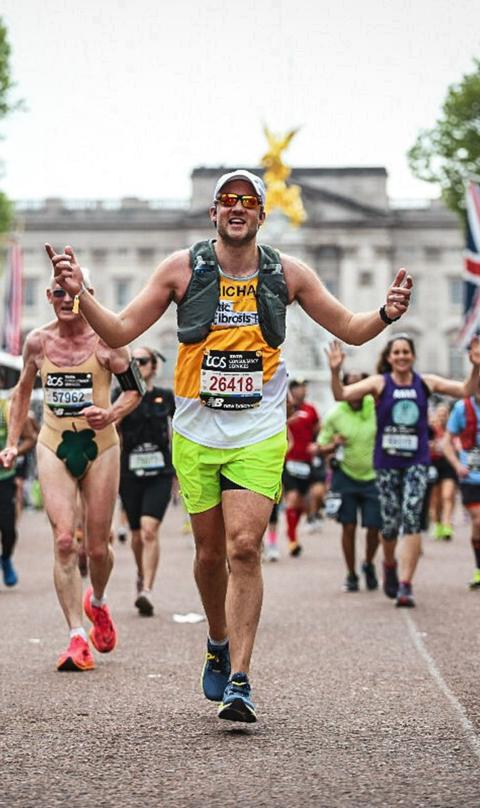A man running in the London marathon, wearing a yellow Cystic Fibrosis Trust vest