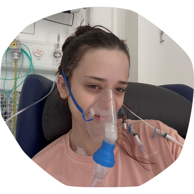 Margot, a young woman with dark hair, in a hospital bed, wearing a mask