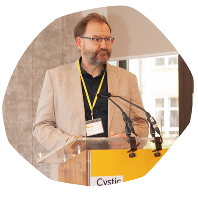 Professor Harrison, a man with a beard and glasses, stanfding at a lectern as he speaks at a Trust conference