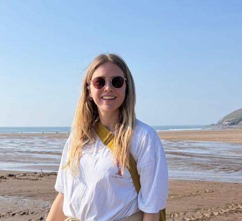 Lucy stands on a beach, smiling at the camera