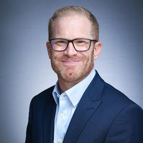 Marks smiles directly at the camera in a professional headshot