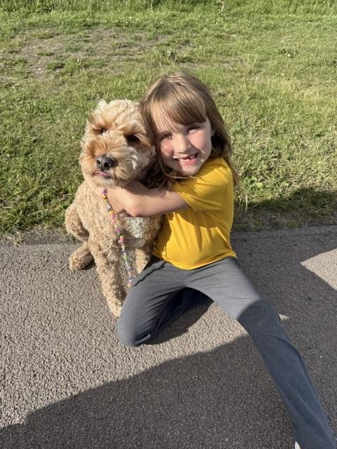 Piper is wearing a yellow shirt, and sits on the ground hugging her dog