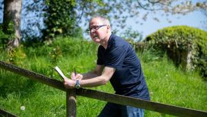 Man in navy shirt looks over a fence facing a field