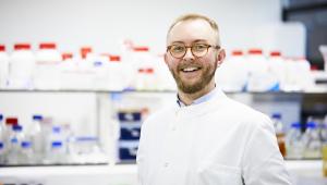 Man in lab coat and glasses smiles at camera