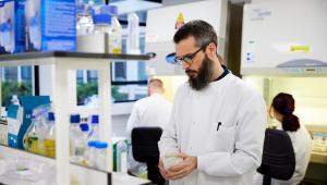 Man in lab coat is inspecting a jar of liquid