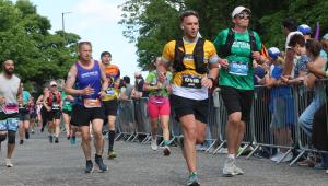 A man running in a marathon, wearing a yellow Cystic Fibrosis Trust vest