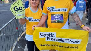 a lady and a man wearing yellow cystic fibrosis tops, holding a yellow foam finger and yellow cystic fibrosis banner